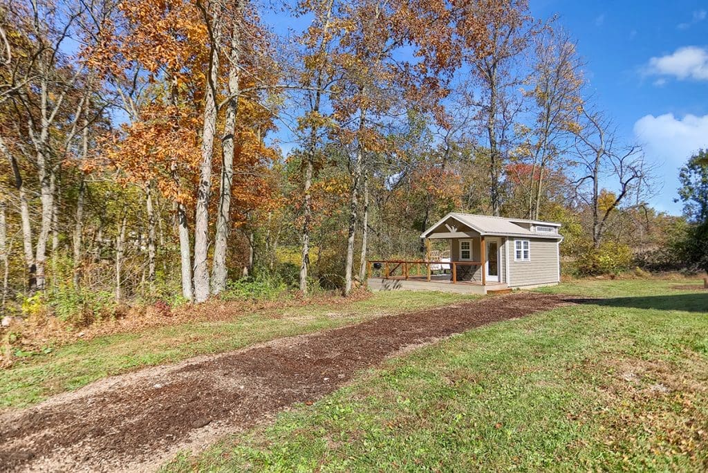 A cabin nestled by nature at the end of a dirt path surrounded by trees.