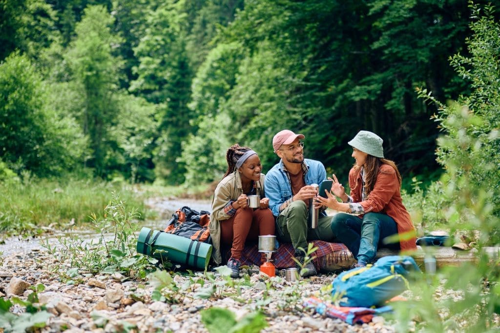 three people with camping gear sitting outside